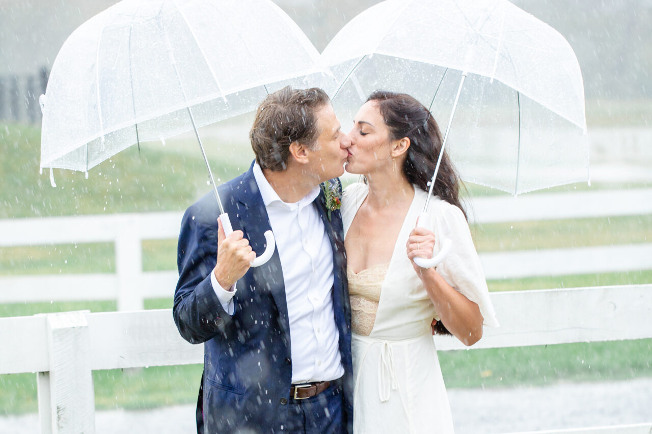 elopement couple kissing in pouring rain under two bubble umbrellas