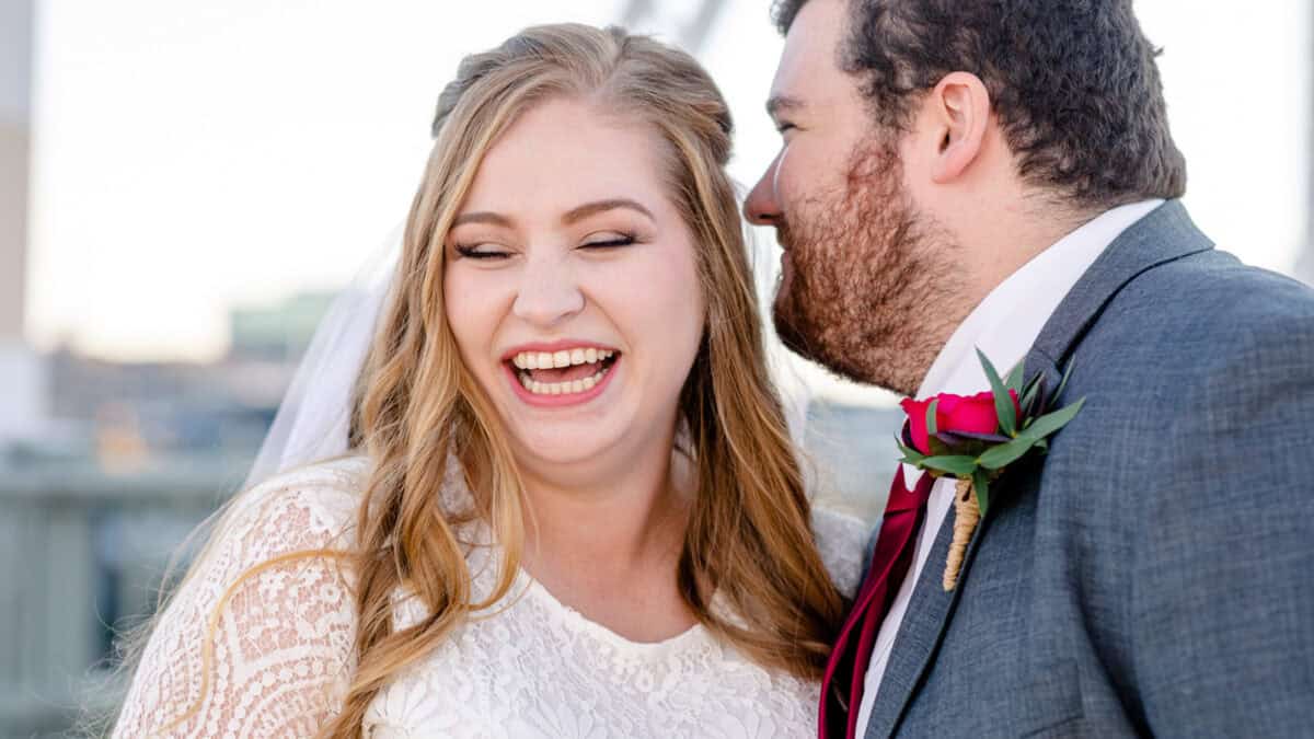 Bride laughs as her groom whispers in her ear.
