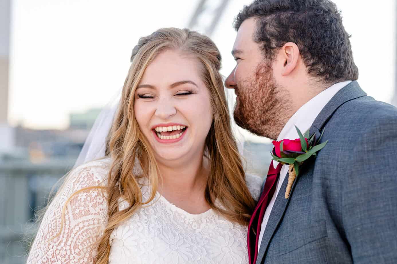 Bride laughs as her groom whispers in her ear.