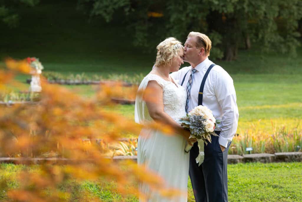 A just-married couple embraces near autumn foliage of ornamental trees at Ellington Agricultural Center