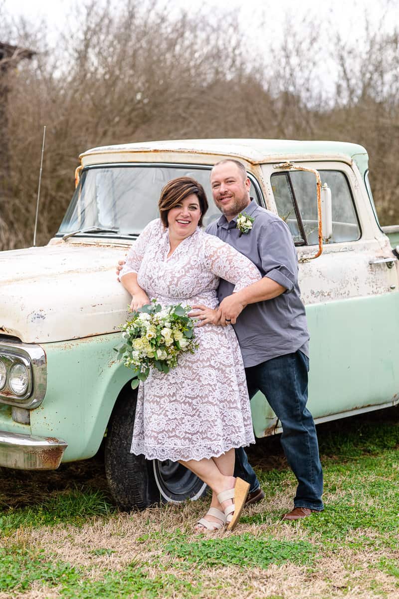 couple pose next to antique car after getting married