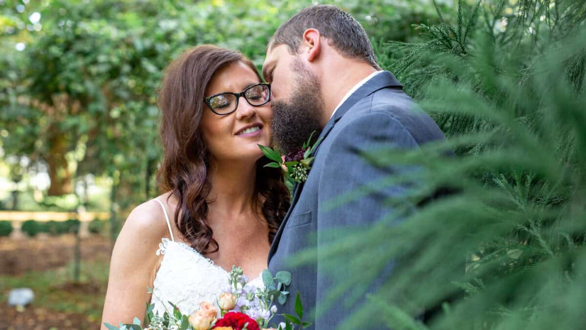 bride kissed by groom on the cheek standing in a garden
