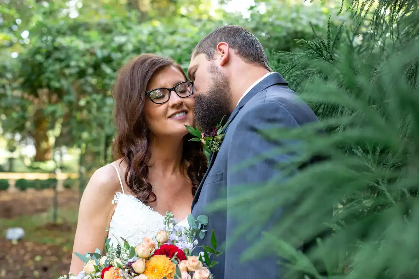 bride kissed by groom on the cheek standing in a garden